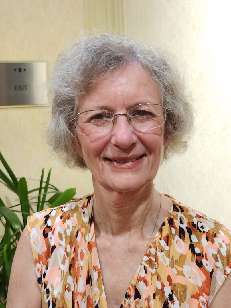 A woman with grey hair wearing glasses and a floral shirt.