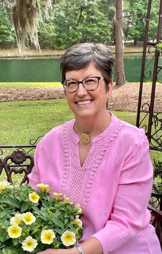 A woman in glasses and pink shirt holding flowers.