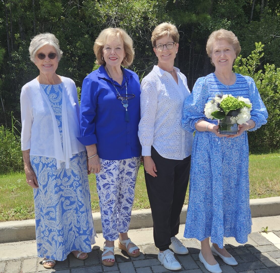 Four women standing next to each other holding a bouquet of flowers.