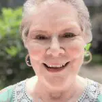 A smiling elderly woman wearing hoop earrings and a light-colored top.