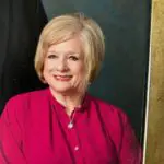A smiling woman in a red blouse with blonde hair.