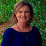 A smiling woman with blonde hair wearing a blue top outdoors.