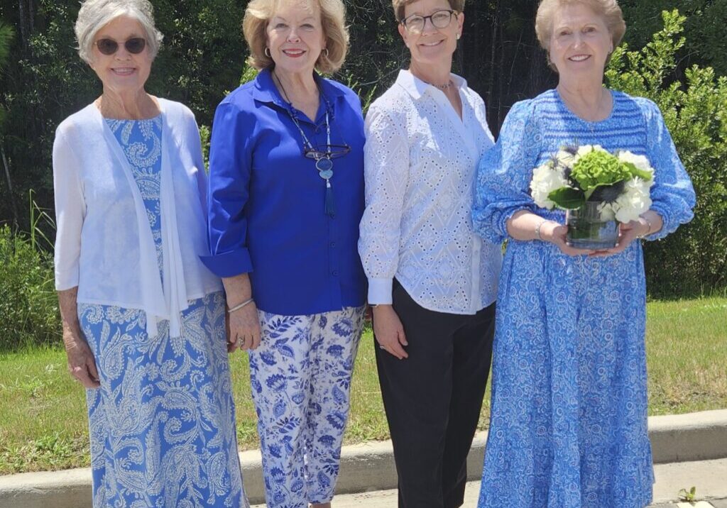 Four women standing next to each other holding a bouquet of flowers.